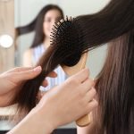 208909578-woman-combing-friend-s-hair-with-cushion-brush-indoors-closeup