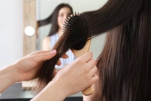 208909578-woman-combing-friend-s-hair-with-cushion-brush-indoors-closeup